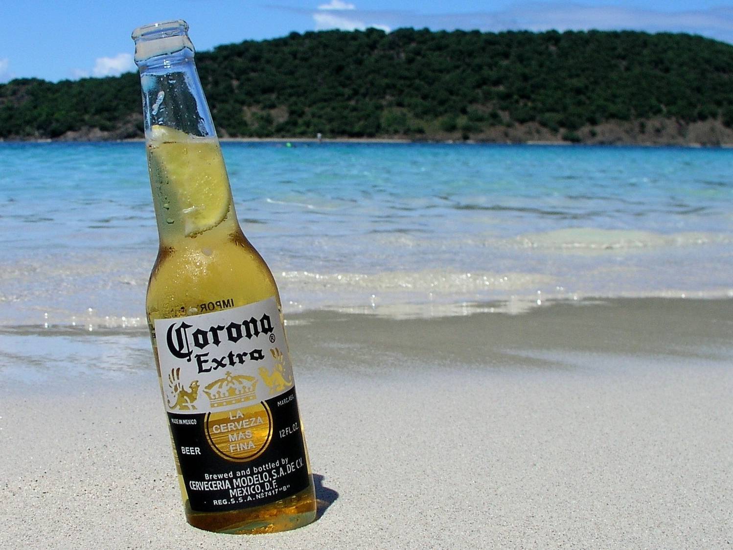 Bottle of Corona beer on a white sand beach with turquoise sea in background
